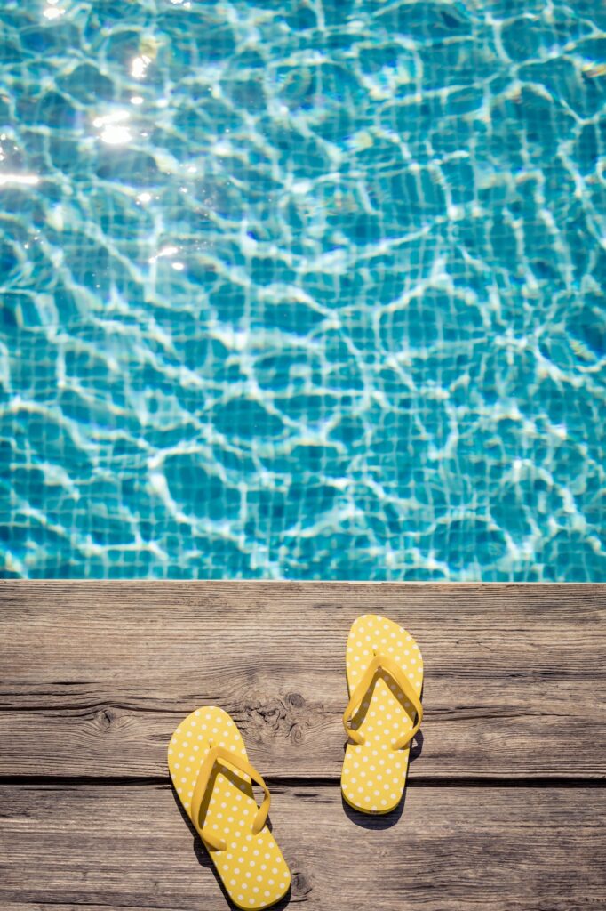 Flip-flops on wooden background near swimming pool